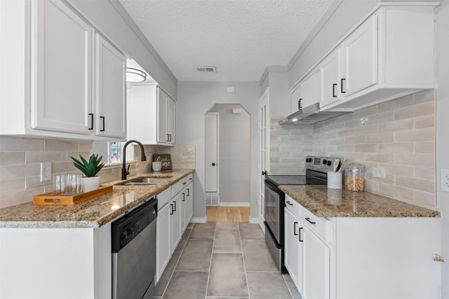 Kitchen with appliances with stainless steel finishes, arched walkways, under cabinet range hood, tasteful backsplash, and white cabinets | Image 12