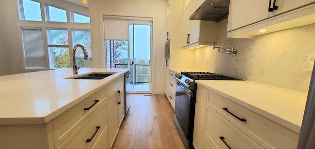 Kitchen featuring light wood-type flooring, under cabinet range hood, white cabinets, a sink, and black range with gas cooktop | Image 4