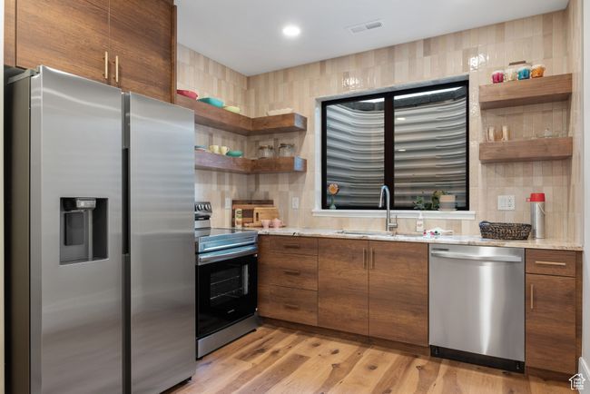 Kitchen featuring appliances with stainless steel finishes, open shelves, brown cabinets, light wood finished floors, and decorative backsplash | Image 58