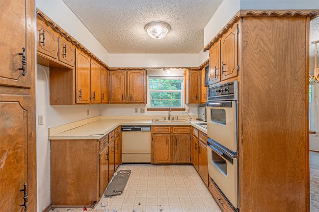 Kitchen featuring white double oven, brown cabinetry, a sink, a textured ceiling, and dishwashing machine | Image 26