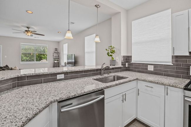 Kitchen with light stone counters, white cabinetry, a sink, appliances with stainless steel finishes, and a ceiling fan | Image 20