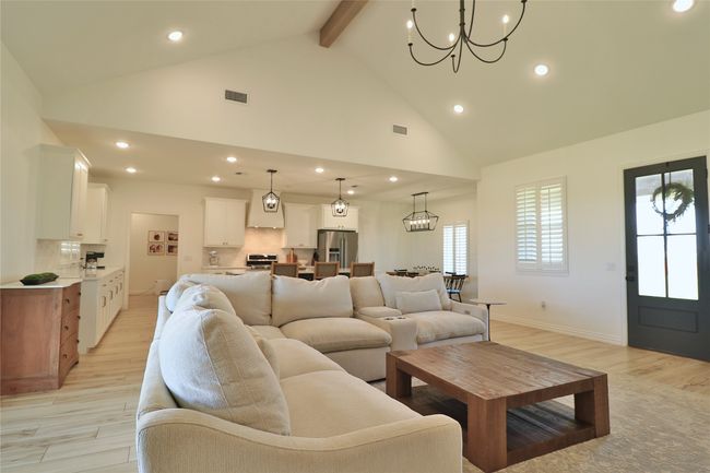Living area with high vaulted ceiling, a notable chandelier, beam ceiling, visible vents, and recessed lighting | Image 8