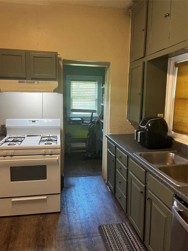 Kitchen featuring stove, dishwasher, dark countertops, a sink, and extractor fan | Image 7