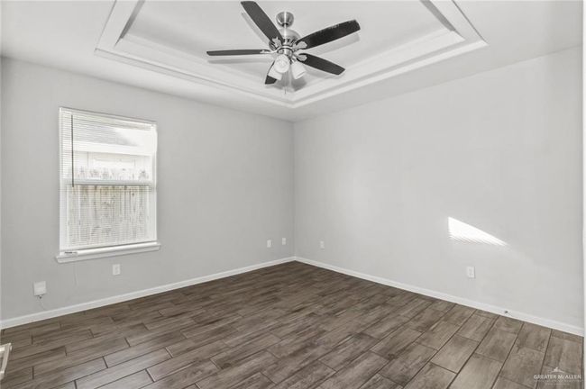 Empty room featuring a tray ceiling, dark wood-style floors, and a ceiling fan | Image 5
