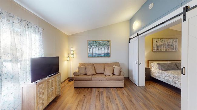 Living area with a barn door, vaulted ceiling, wood finished floors, and healthy amount of natural light | Image 17