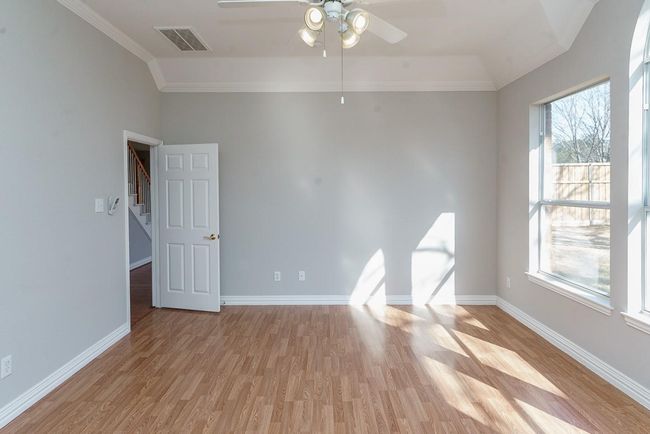Empty room with a ceiling fan, visible vents, baseboards, light wood-type flooring, and crown molding | Image 13