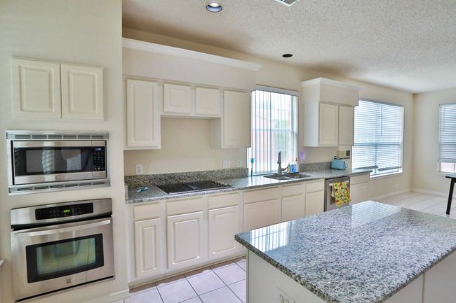 Kitchen with appliances with stainless steel finishes, light tile patterned floors, light stone countertops, white cabinets, and a textured ceiling | Image 6