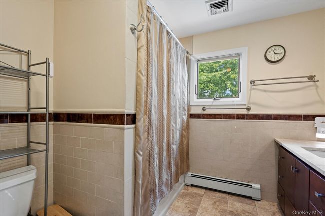 Full bathroom with tile walls, a baseboard heating unit, a wainscoted wall, and vanity | Image 16