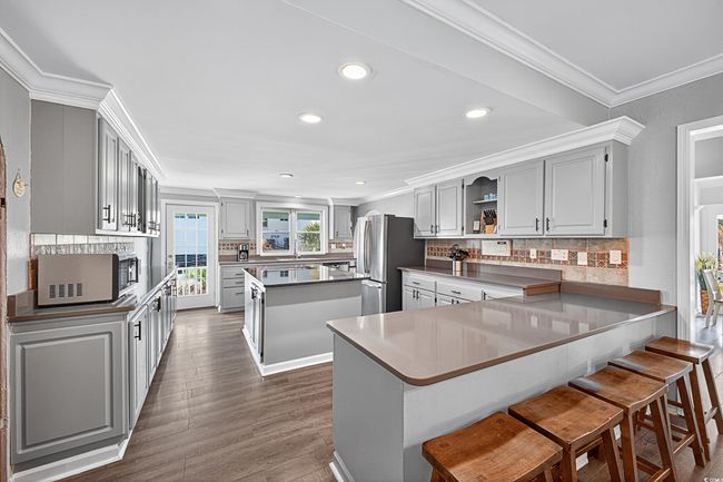 Kitchen featuring freestanding refrigerator, a kitchen island, tasteful backsplash, ornamental molding, and open shelves | Image 33