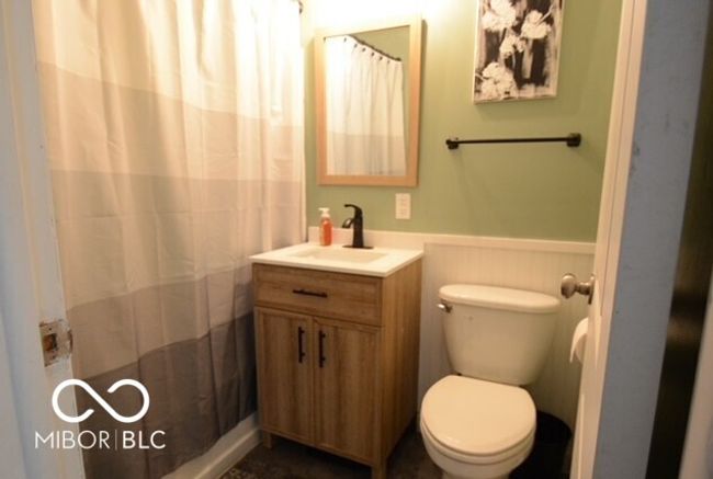 bathroom with a shower with curtain, a wainscoted wall, vanity, and toilet | Image 15