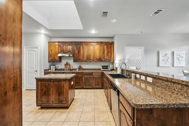 Kitchen featuring a peninsula, under cabinet range hood, light tile patterned flooring, a center island, and recessed lighting | Image 20