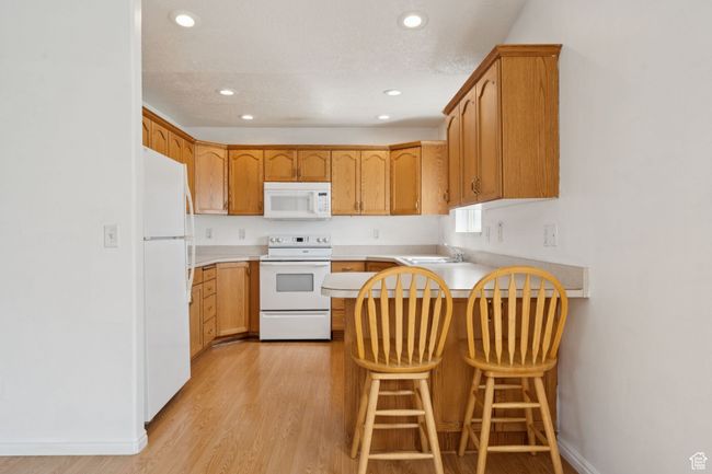 Kitchen with white appliances, a peninsula, light wood-style flooring, recessed lighting, and light countertops | Image 9