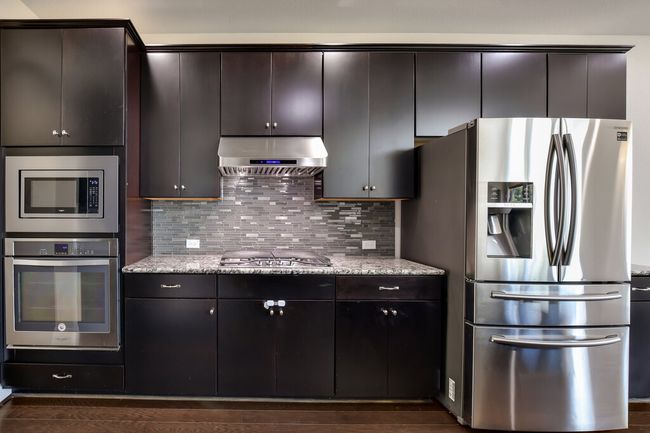 Kitchen with appliances with stainless steel finishes, extractor fan, decorative backsplash, dark brown cabinetry, and light stone countertops | Image 11