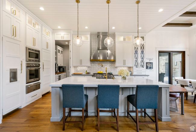 Kitchen with tasteful backsplash, dark wood-style flooring, wall chimney range hood, appliances with stainless steel finishes, and a warming drawer | Image 24