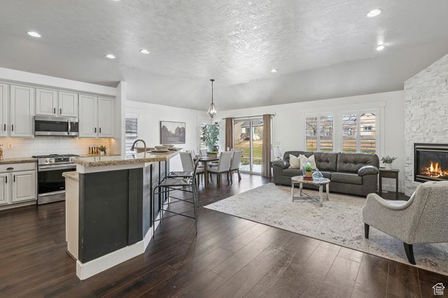 Great room with dark hardwood / wood-style flooring, plenty of natural light, lofted ceiling, a fireplace, & plantation shutters. | Image 5
