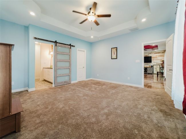 Unfurnished bedroom featuring a barn door, carpet, a raised ceiling, recessed lighting, and ensuite bathroom | Image 18