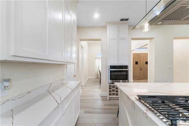 Kitchen with light stone countertops, pendant lighting, light hardwood / wood-style flooring, stainless steel oven, and white cabinets | Image 17