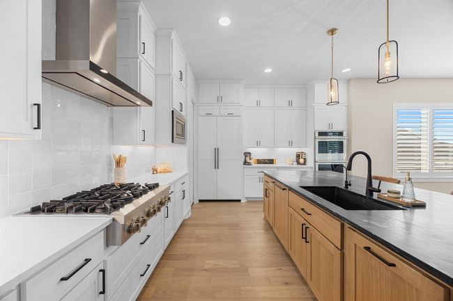 Kitchen featuring light wood finished floors, wall chimney exhaust hood, stainless steel appliances, recessed lighting, and hanging light fixtures | Image 8