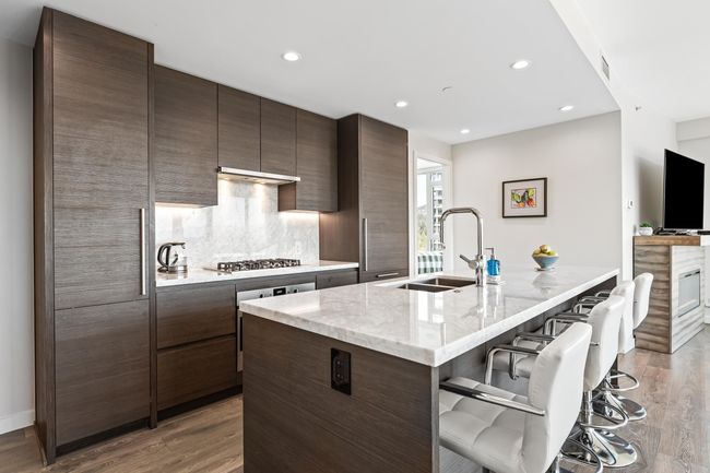 Kitchen with wood finished floors, a sink, a breakfast bar, dark brown cabinetry, and backsplash | Image 4