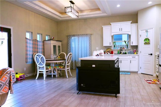 Kitchen with a kitchen island, light countertops, white cabinets, and a raised ceiling | Image 10