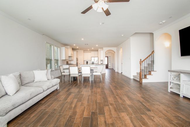 Living area with arched walkways, ornamental molding, a ceiling fan, dark wood finished floors, and stairs | Image 7