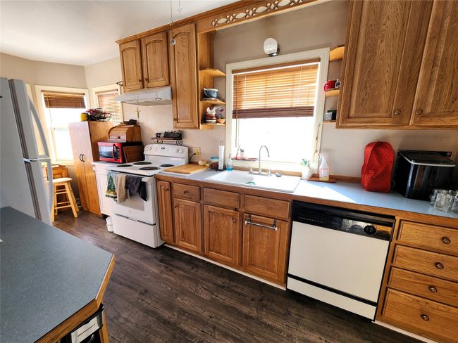 Kitchen with dark wood-style flooring, white appliances, under cabinet range hood, a sink, and a healthy amount of sunlight | Image 19