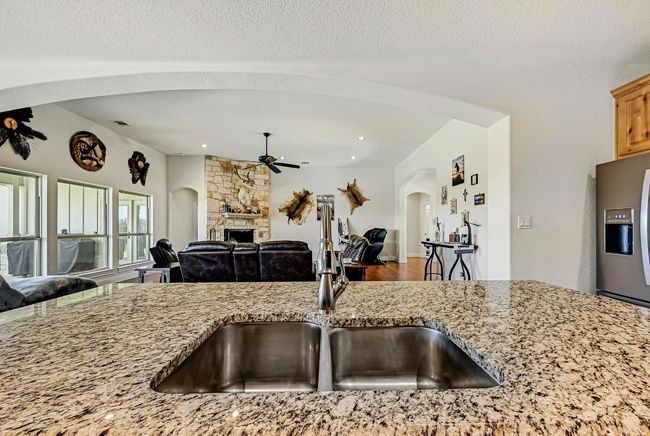 Kitchen with ceiling fan, open floor plan, stainless steel refrigerator with ice dispenser, arched walkways, and light stone counters | Image 11