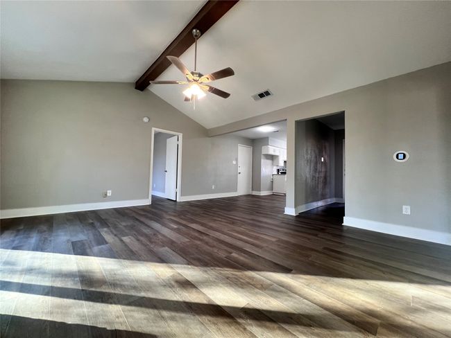 Unfurnished living room with dark wood-type flooring, vaulted ceiling with beams, and ceiling fan | Image 13