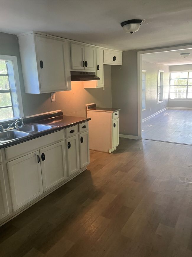 Kitchen featuring a sink, wood finished floors, white cabinetry, range hood, and dark countertops | Image 7