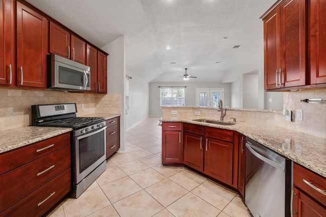 Kitchen featuring appliances with stainless steel finishes, lofted ceiling, dark brown cabinets, backsplash, and ceiling fan | Image 13