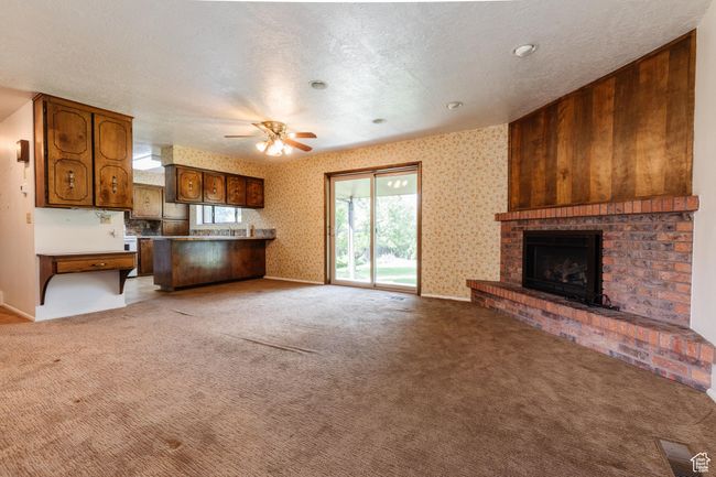Unfurnished living room featuring a ceiling fan, a brick fireplace, light colored carpet, wallpapered walls, and a textured ceiling | Image 6