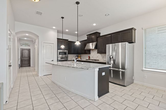 Kitchen with stainless steel appliances, under cabinet range hood, arched walkways, tasteful backsplash, and light stone countertops | Image 6