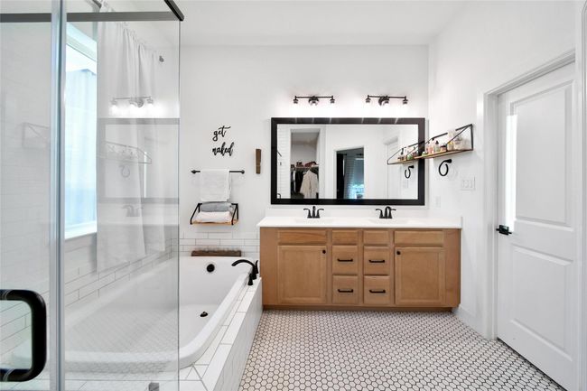 This bathroom features a modern design with a glass-enclosed shower, a bathtub, a large mirror above a double vanity with wooden cabinets, and sleek black fixtures. The hexagonal tile flooring adds a stylish touch. | Image 32