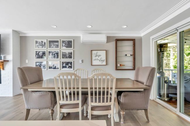 Dining area with a wall mounted air conditioner, wood finished floors, ornamental molding, and a fireplace | Image 13