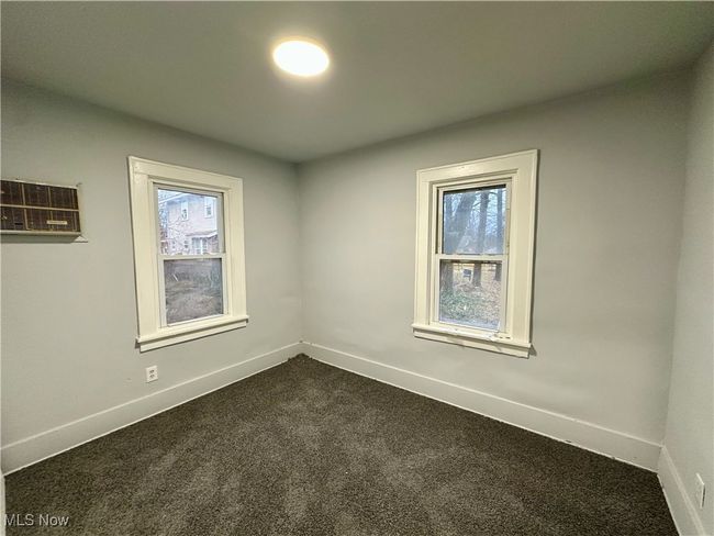 Spare room with dark colored carpet, baseboards, and an AC wall unit | Image 4