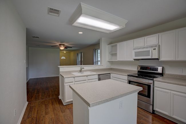 Kitchen featuring appliances with stainless steel finishes, a sink, a peninsula, open shelves, and white cabinets | Image 20