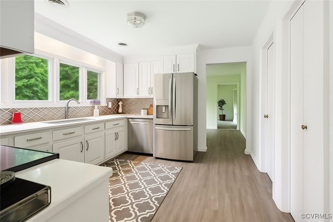 Kitchen with appliances with stainless steel finishes, tasteful backsplash, white cabinets, and light wood-type flooring | Image 5