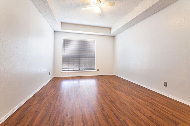 Empty room featuring a raised ceiling, ceiling fan, dark wood-type flooring, and a textured ceiling | Image 7