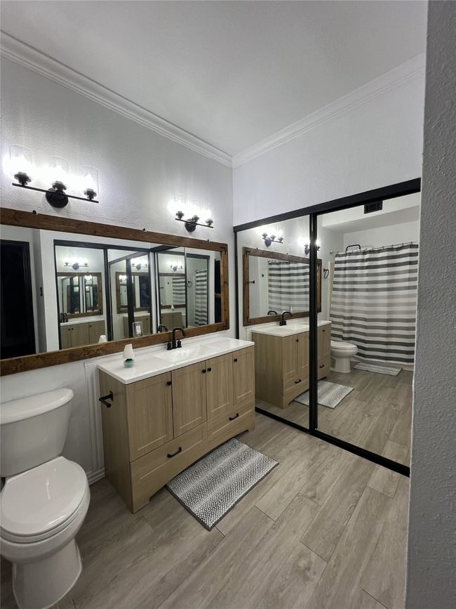 Full bath with wood finished floors, toilet, ornamental molding, a sink, and two vanities | Image 9