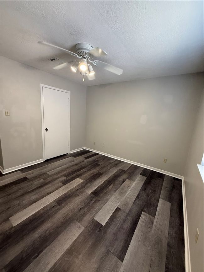 Empty room with a textured ceiling, dark wood-style flooring, and ceiling fan | Image 8