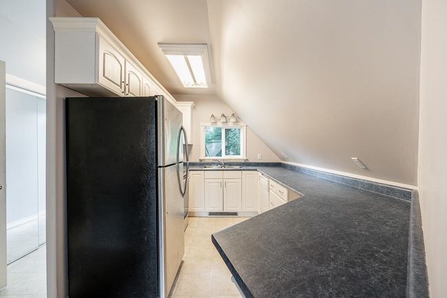 Kitchen featuring light tile patterned flooring, dark countertops, a sink, vaulted ceiling, and freestanding refrigerator | Image 29