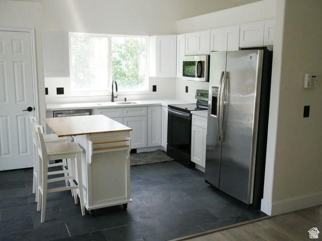 Kitchen with stainless steel appliances, white cabinets, a breakfast bar, and light countertops | Image 9
