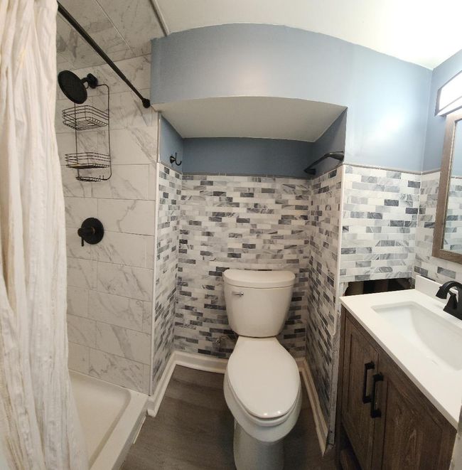 Full bathroom featuring toilet, vanity, tile walls, and a shower stall | Image 11