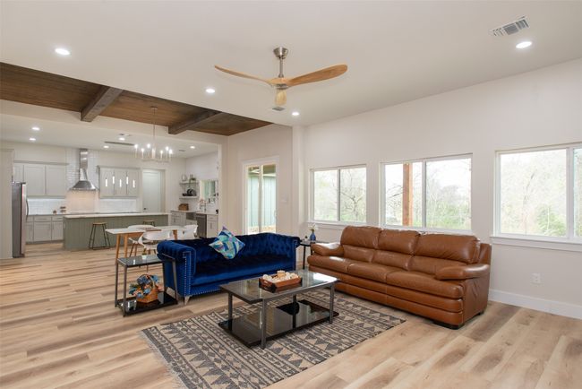 Living room with beamed ceiling, ceiling fan with notable chandelier, and light hardwood / wood-style floors | Image 17