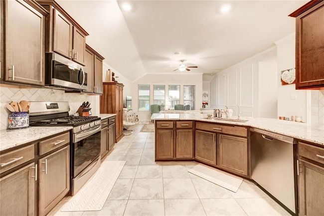 Open concept kitchen with dark wood cabinets, farmhouse sink, gas stovetop and oven, and granite countertops | Image 8