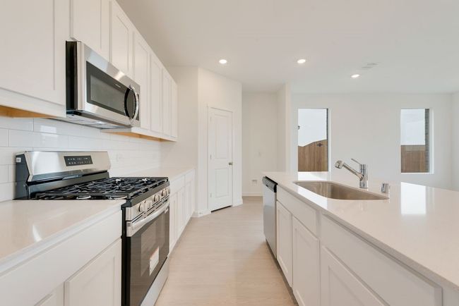Kitchen featuring appliances with stainless steel finishes, a sink, backsplash, white cabinetry, and recessed lighting | Image 11