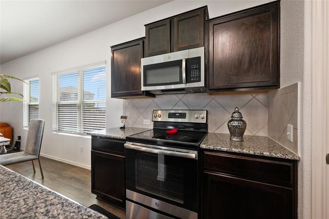 Kitchen with appliances with stainless steel finishes, dark wood-style floors, decorative backsplash, dark stone counters, and dark brown cabinets | Image 9