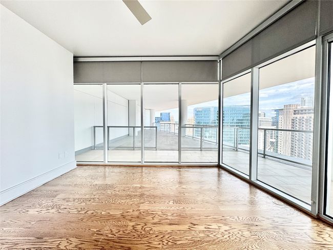 Empty room featuring a city view, wood finished floors, floor to ceiling windows, a ceiling fan, and baseboards | Image 10