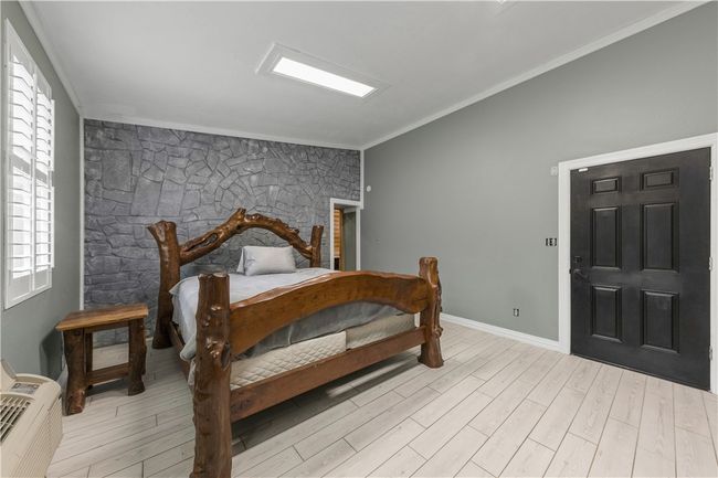 downstairs primary Bedroom with wood look tile flooring, crown molding, and multiple windows | Image 23