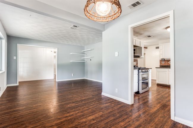 Empty room with dark wood-style floors, baseboards, and a chandelier | Image 11